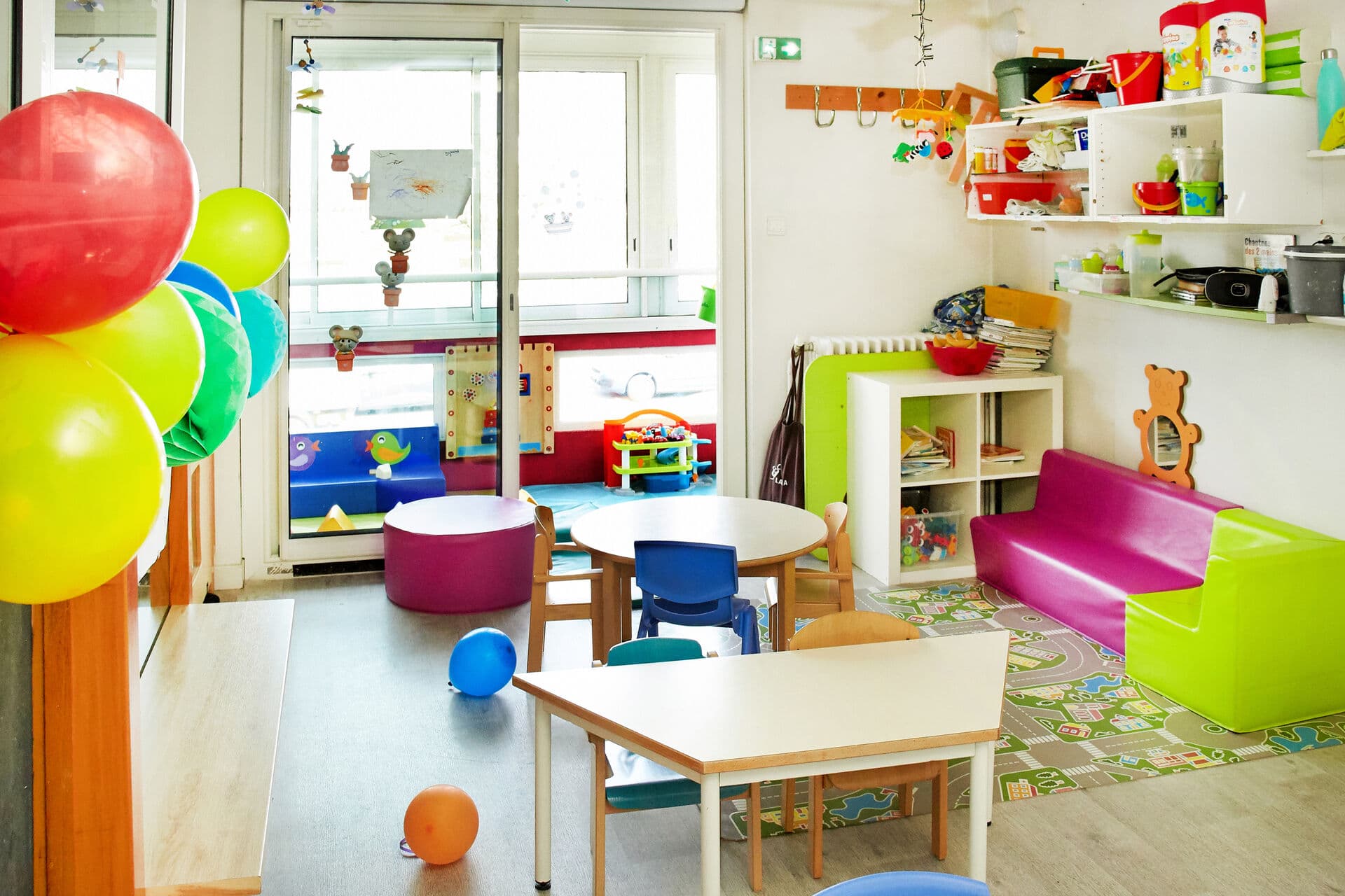 Salle de vie colorée avec ballons, petites tables et coin lecture